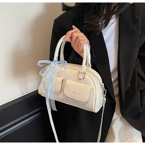 Detail view of cream Boston bag with front flap pockets and elegant blue checkered ribbon