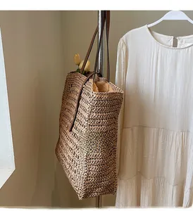 Detail of hand-woven straw tote texture with brown leather strap hanging against white wall