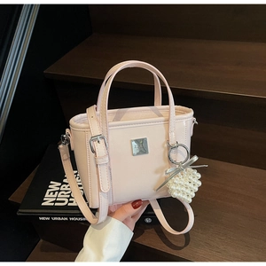 Dettaglio borsa a secchiello rosa chiaro in pelle lucida con targa e ciondolo di perle
