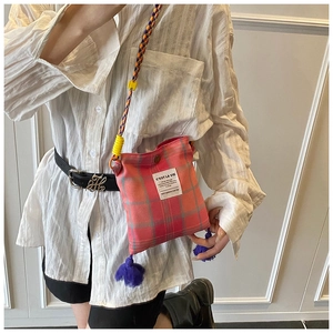 Detail of plaid canvas crossbody bag with purple tassel and colorful woven strap