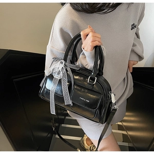 Detail of black glossy Boston bag featuring cargo pockets and lace bow decoration