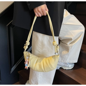 Détail du sac croissant jaune avec texture litchi, chaîne de perles et pendentif poupée