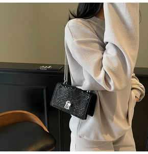 Detail of black snake-embossed small square bag with silver metal lock and chain strap