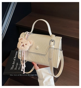 Detail view of cream white PU leather crossbody bag with a cute plush bear charm