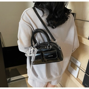 Detail of black patent leather Boston bag featuring lace bow and small front pockets