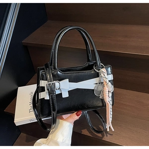 Dettaglio borsa in vernice nera con fiocco bianco, fibbia argento e ciondolo da tennis
