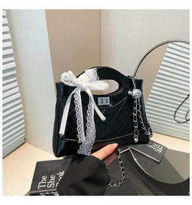 Detail of black quilted bucket bag featuring a white lace bow and silver chain strap