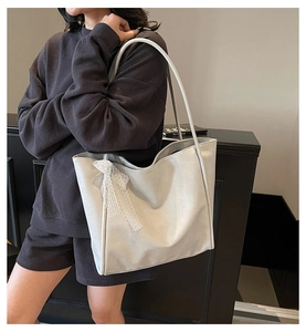 Detailed side view of a large silver tote bag featuring a white lace bow charm on model