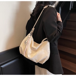 Detail of cream shoulder bag with knotted handle and tassel ornament on soft material