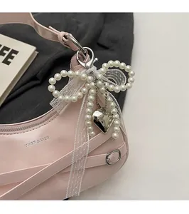 Detail of light pink patent leather hobo bag with pearl bow and silver heart pendant