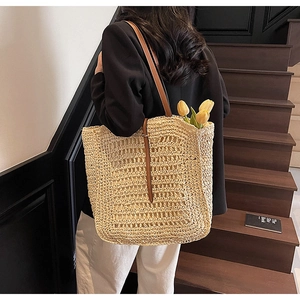 Large woven straw tote bag with brown leather straps shown in a scenic outdoor setting