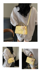 Detail view of yellow square crossbody bag with top handle and cute bear plush charm