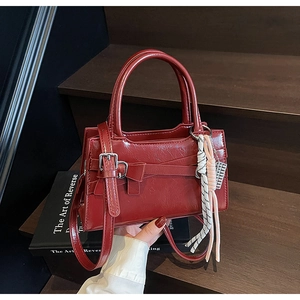 Dettaglio della borsa in pelle bordeaux con fibbia a fiocco e tracolla su scale