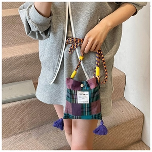 Detail of plaid crossbody bag with colorful woven rope strap and purple tassel accents