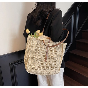 Close-up of woven straw tote bag featuring brown leather shoulder straps and tulip detail