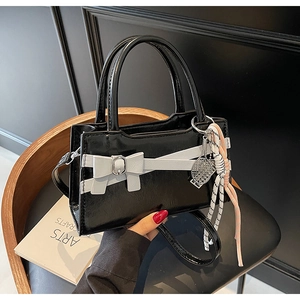 Dettaglio borsa in pelle verniciata nera con fiocco bianco e ciondolo da tennis alla moda