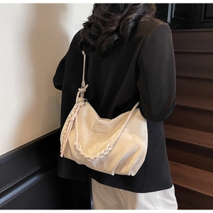 Detail of a creamy beige oversized hobo bag featuring a woven handle and tassel charm