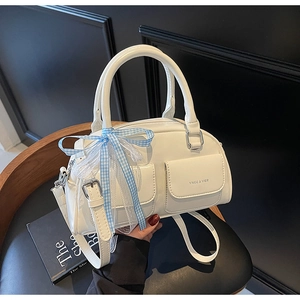 Detail of white Boston bag featuring dual front pockets and blue ribbon bow decoration