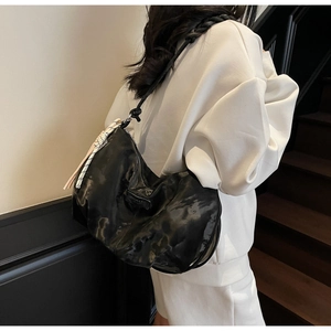 Detail of glossy black tote bag featuring woven rope strap and striped silk scarf charm