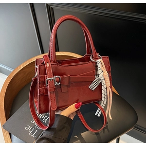 Dettaglio borsa lucida rosso scuro con fiocco decorativo e ciondolo abaco su libri