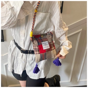 Detail of a patchwork plaid crossbody bag featuring colorful tassels and woven strap