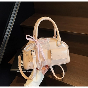 Close-up of beige Boston bag featuring a bow ribbon and dual front pockets with logo detail