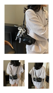 Detail of black patent leather hobo bag with pearl bow charm and lace ribbon accessory