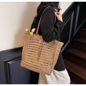 Close-up of woven straw tote bag featuring brown leather straps and fine hollow texture