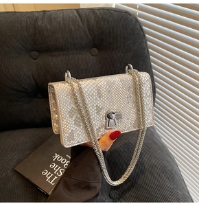 Detail of silver snake-pattern square bag with metallic chain and turn-lock closure