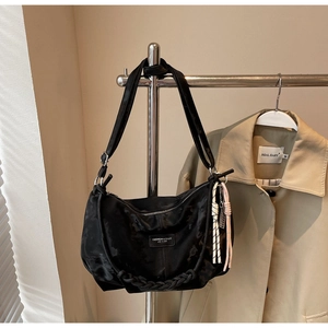 Detail of black crescent hobo bag with woven rope handle accent hanging in a closet