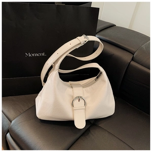 Detail of white pleated moon bag with silver buckle on a black leather sofa