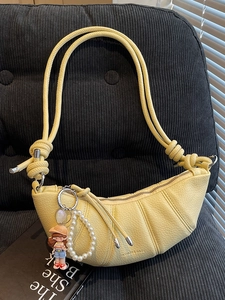 Sac croissant jaune chic avec bandoulière nouée et breloques de poupée perle sur sofa