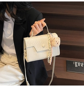 Detail of cream-white wrinkled PU leather bag with cute plush bear charm and woven cord