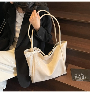 Detail of a beige soft leather tote bag featuring a delicate white lace bow decoration