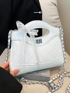 White quilted bucket bag with chain strap and lace bow displayed on a book