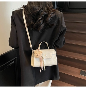 White minimalist square bag with pearl clasp and plush bear charm worn on shoulder