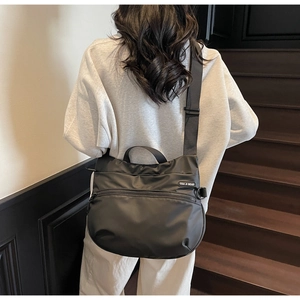 Detail of black nylon crescent tote bag showing top handle and side zipper pocket