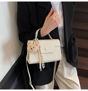 Detail view of the white rectangular crossbody bag with lychee texture and bear charm