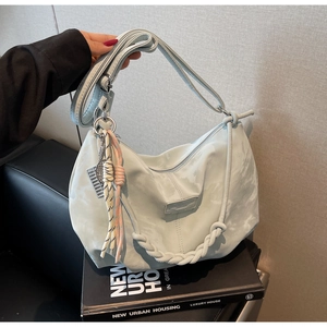 Detail of light blue hobo bag with braided handle and cute feather pendant accessory