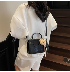Detail of minimalist black leather crossbody bag featuring a cute beige plush bear charm