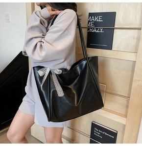 Detail of black faux leather tote bag featuring elegant white lace bow decoration