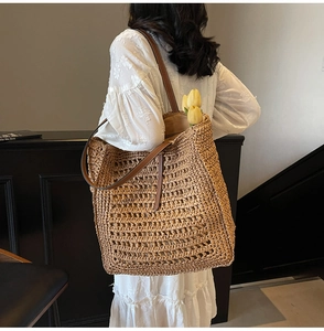 Macro view of large woven straw tote bag detailing hollow weave and leather shoulder strap
