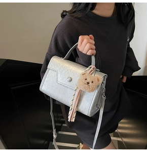 Detail of silver metallic textured crossbody bag with cute plush bear keychain accessory