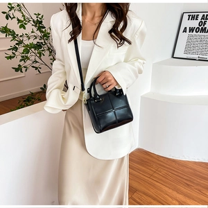 Détail d'un sac à main carré noir avec boucle dorée porté par un mannequin élégant