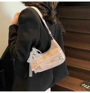 Detail of pale pink crescent underarm bag featuring decorative straps and pearl heart charm