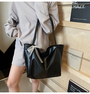 Chic black soft leather tote bag with white lace bow detail shown on a wooden background
