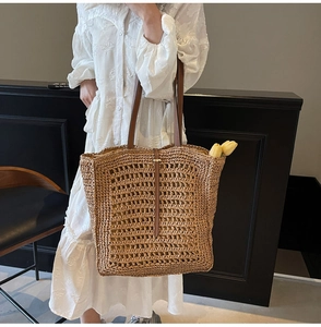 Close-up of the dense straw woven texture and brown leather strap on a large tote bag