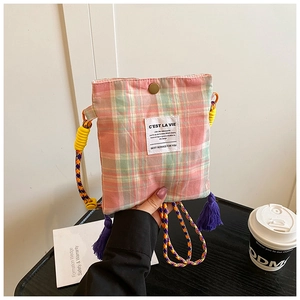 Detail of plaid fabric crossbody bag featuring colorful braided strap and purple tassel charm