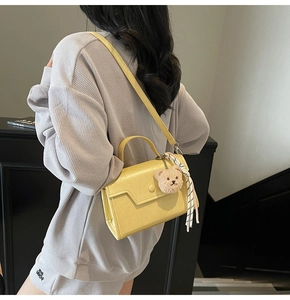 Detail of yellow glossy leather crossbody bag with teddy bear charm and striped scarf