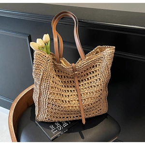 Detail of straw woven tote bag featuring hollow patterns and brown leather straps